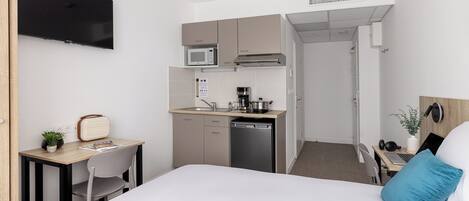 Una habitación de hotel compacta con kitchenette, cama, escritorio y televisión.