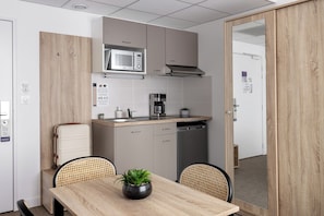 Une petite cuisine équipée d’un four à micro-ondes, d’une machine à café et d’un petit évier. On y trouve également une table à manger avec des chaises et une plante en pot.