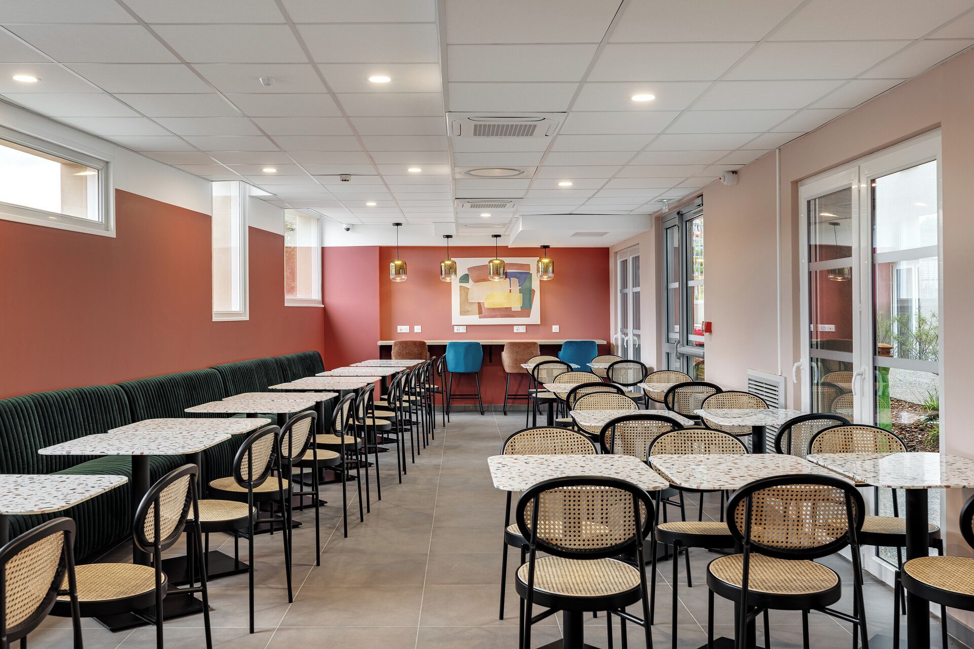 Un restaurant avec des banquettes et des tables, un mur rouge et une grande fenêtre.
