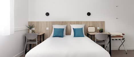 Una habitación de hotel moderna con una cama grande, dos mesitas de noche, un escritorio con una silla y una pequeña mesa con una planta.