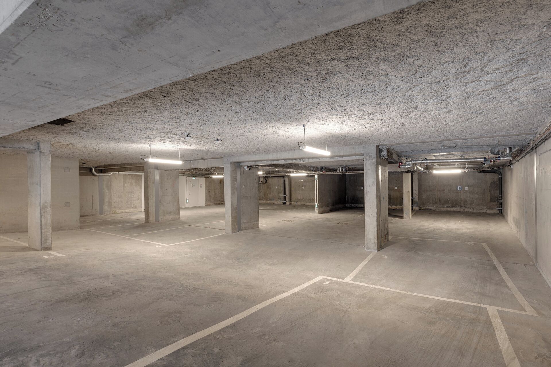 A spacious underground parking area with concrete pillars and marked parking spaces.