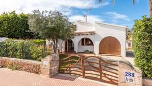 A white building with a large wooden door, a stone gate, and a number plaque. - Tolo 3 bedroom villa, Cala'n Blanes (Ciutadella de Menorca)
