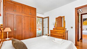 A hotel room with a large bed, wooden wardrobe, dresser, and a mirror. - Tolo 3 bedroom villa, Cala'n Blanes (Ciutadella de Menorca)