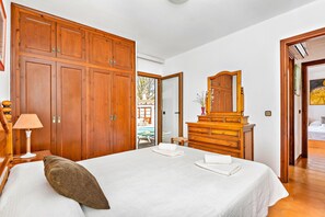 A hotel room with a large bed, wooden wardrobe, dresser, and a mirror. - Tolo 3 bedroom villa, Cala'n Blanes (Ciutadella de Menorca)