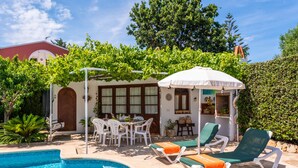 A poolside area with lounge chairs, a table, and a pergola with vines. - Tolo 3 bedroom villa, Cala'n Blanes (Ciutadella de Menorca)