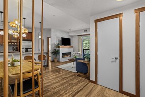 Eine moderne Küche mit Holzausbau, ein Essbereich mit einem Holztisch und -stühlen, ein Wohnzimmer mit einer Couch und Fernseher sowie ein Kamin.