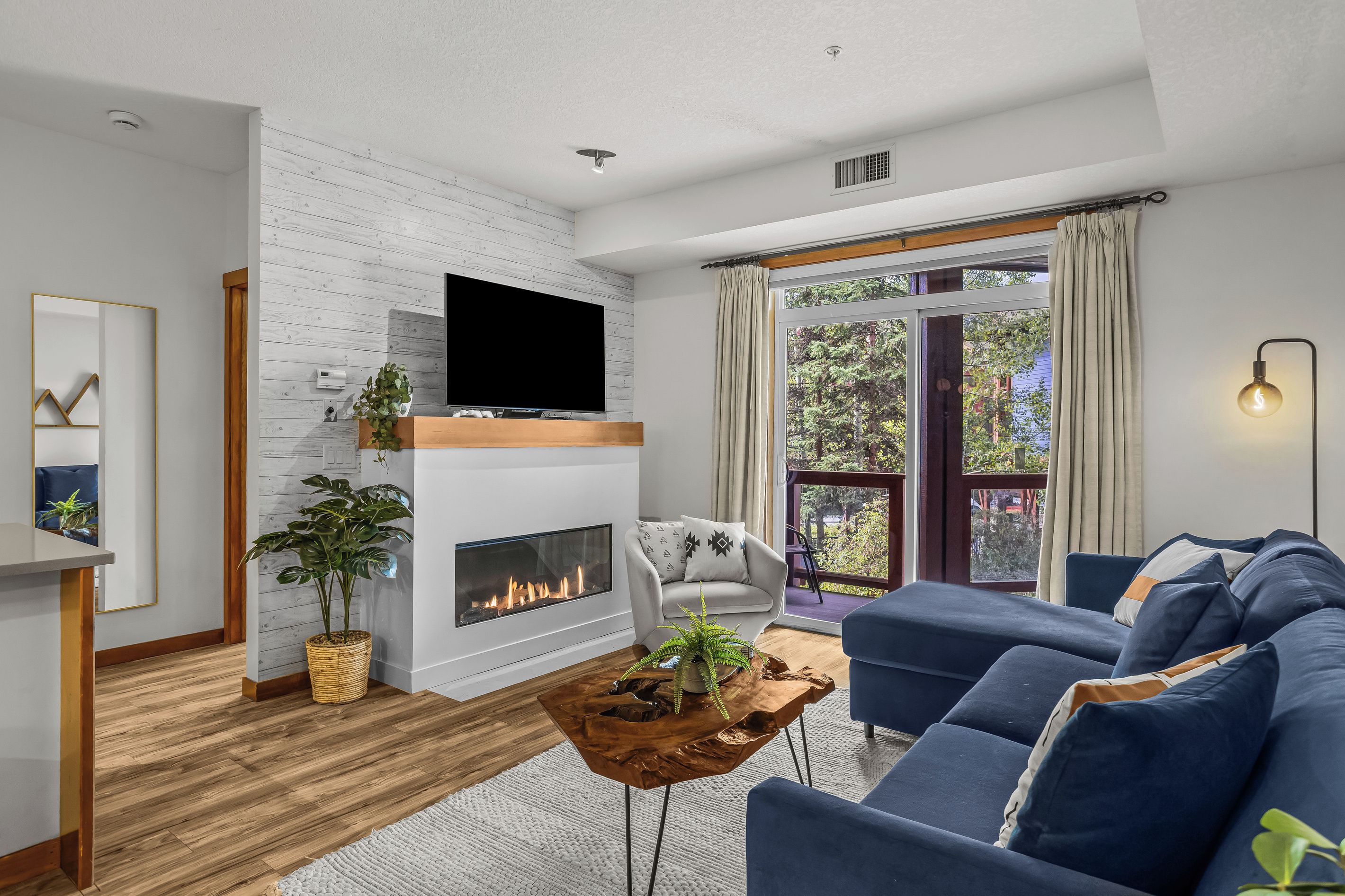A modern living room with a fireplace, a television, a sofa, and a view of the outdoors.