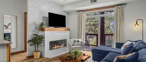 A modern living room with a fireplace, a television, a sofa, and a view of the outdoors.