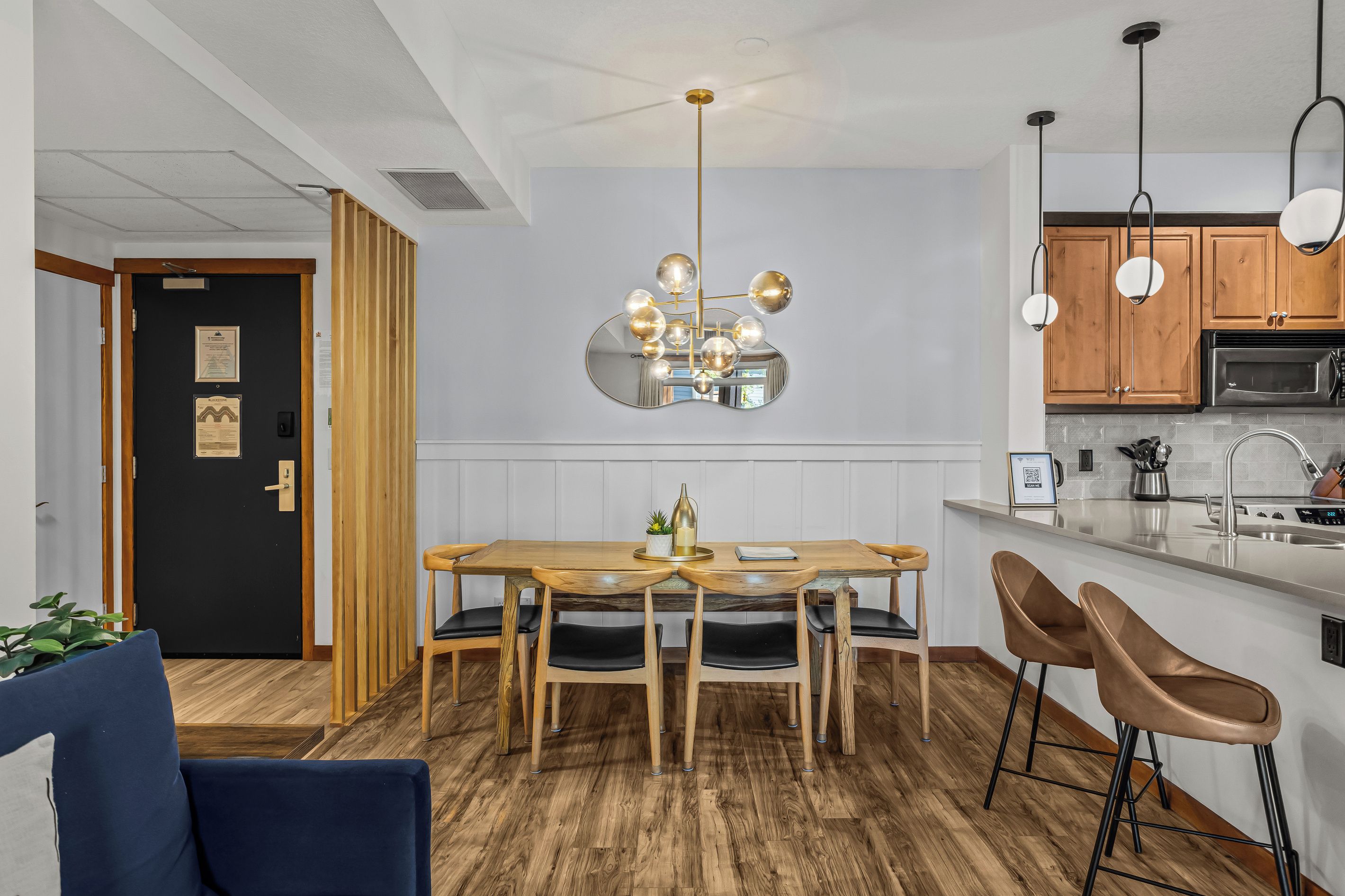 A modern kitchen with a central island, wooden dining table, and bar stools.