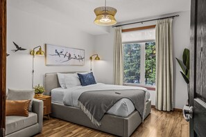 Ein modernes Schlafzimmer mit einem großen Bett, zwei Nachttischlampen, einem Fenster mit Vorhängen und einem Wandbild.