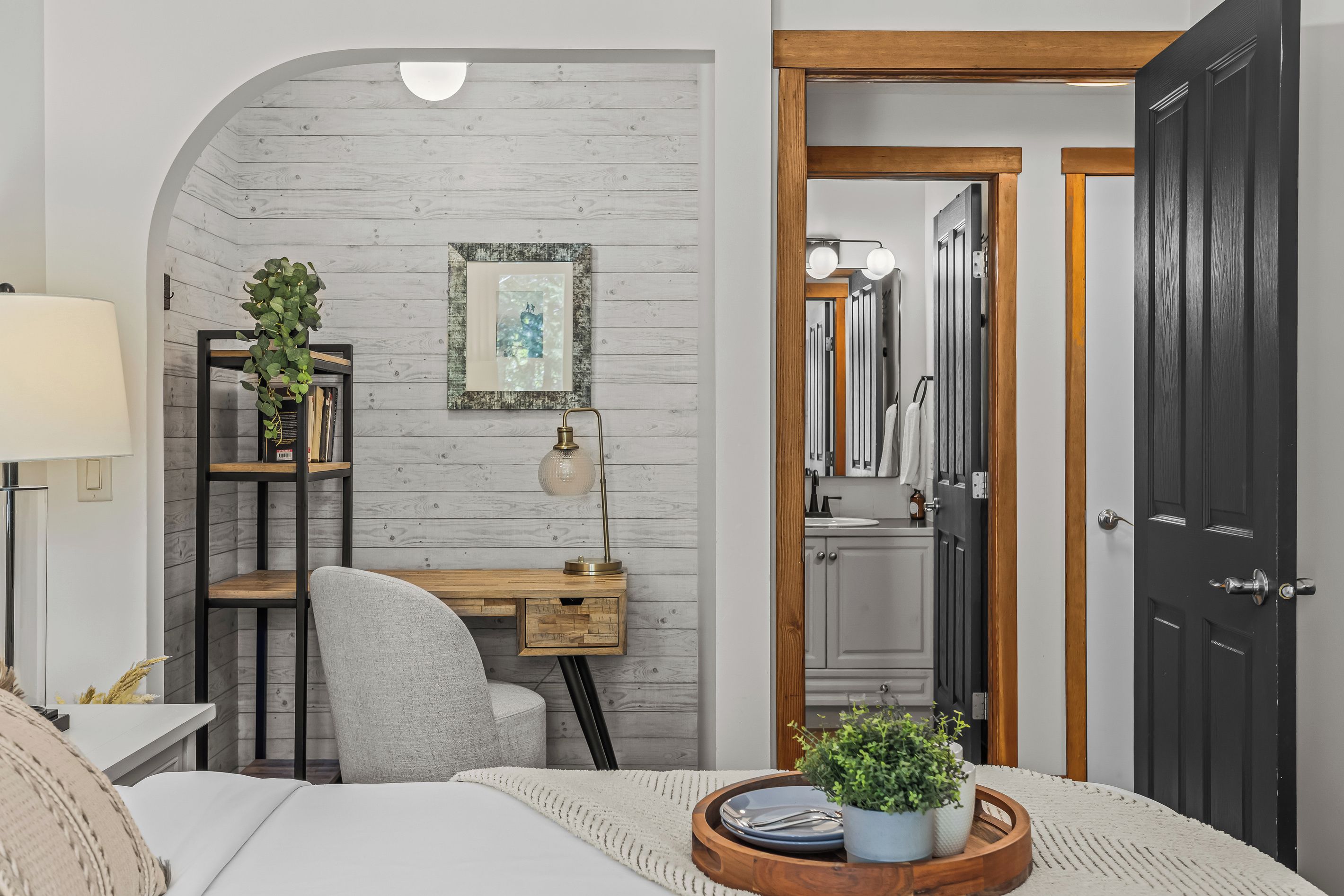 A bedroom with a bed, a desk, a chair, a lamp, a plant, and a door.