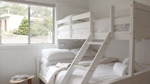 A bunk bed with white bedding, a small wooden table, and a window with a view of greenery.