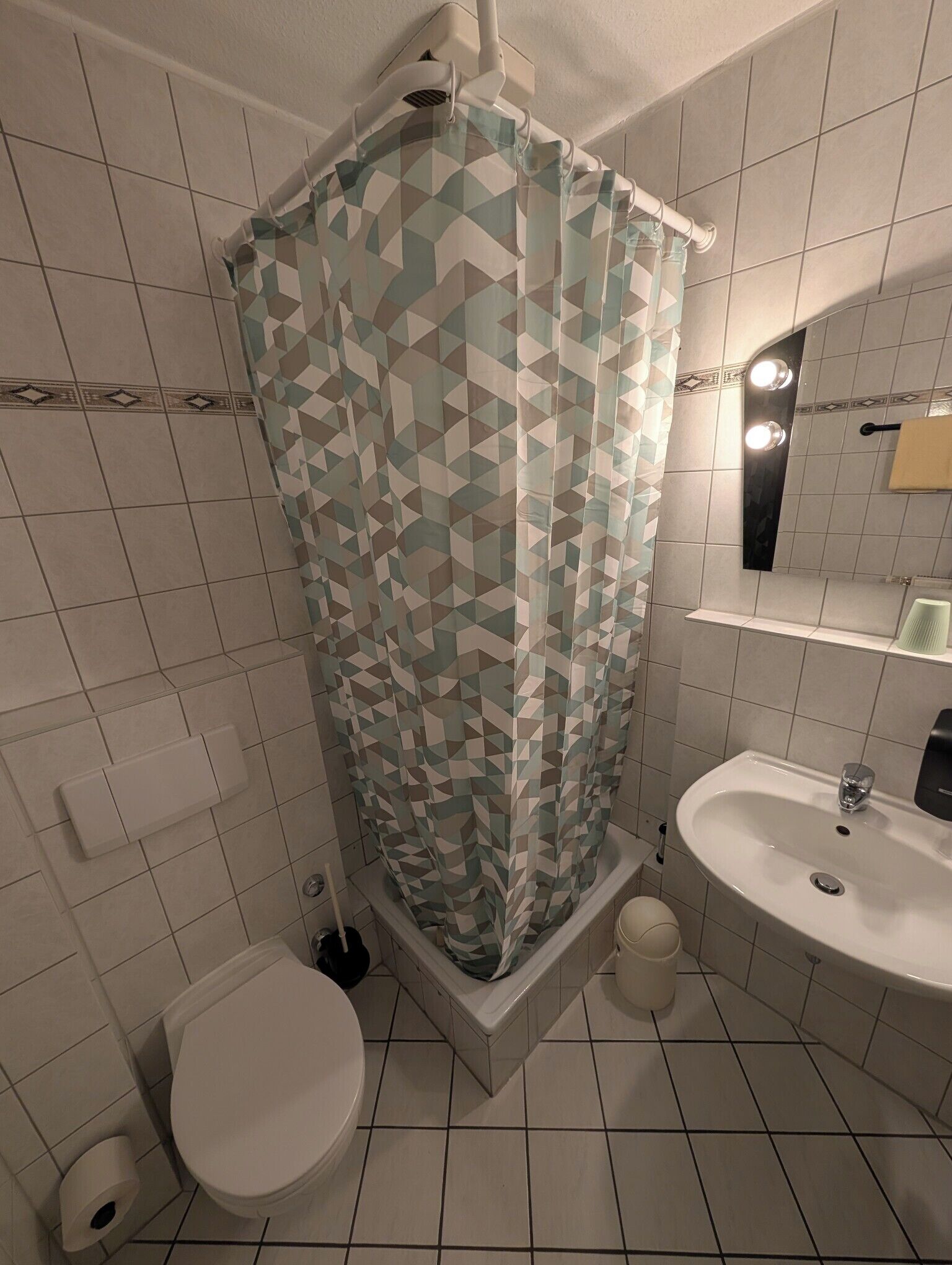 A bathroom with a shower curtain, toilet, sink, and a mirror above the sink.