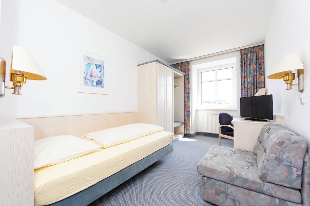 A hotel room with a bed, a sofa, a TV, and a painting on the wall.