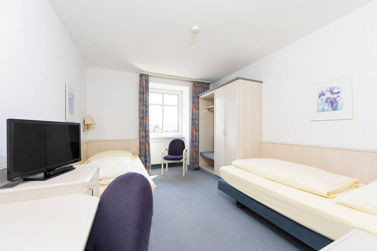 A hotel room with a bed, a TV, a chair, and a wardrobe.