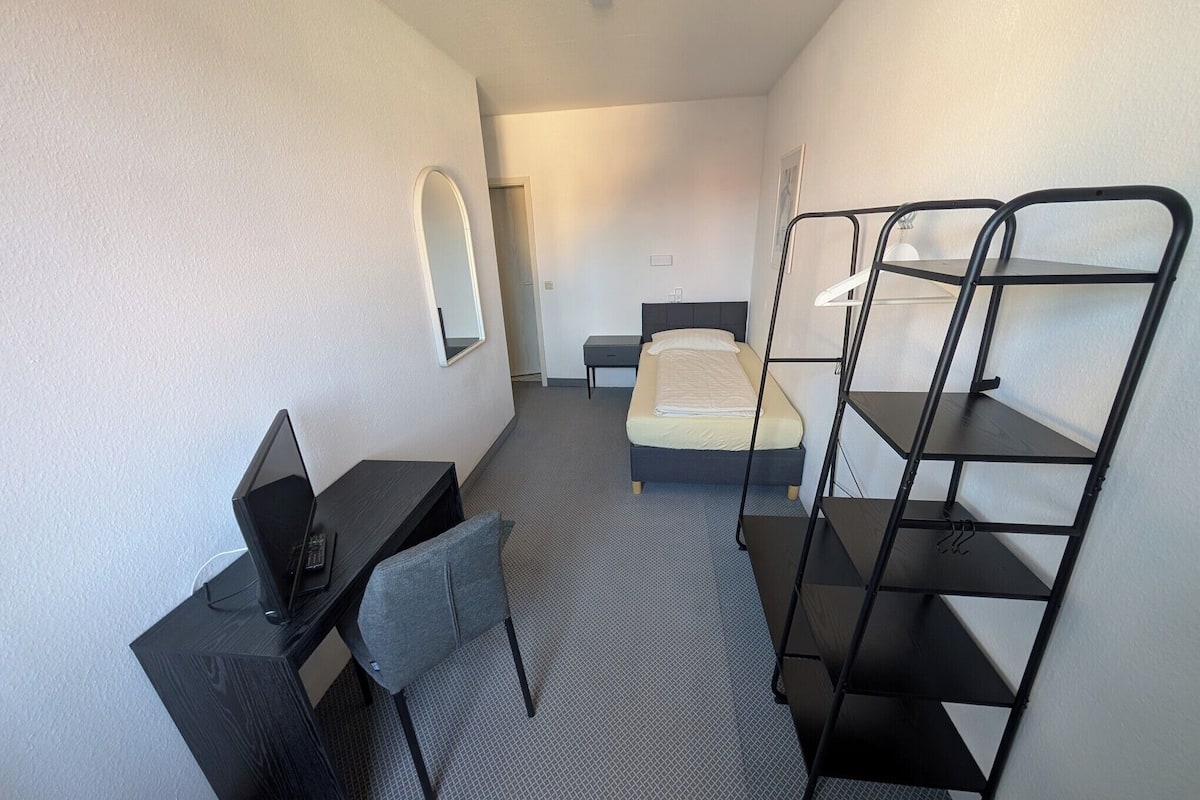 A hotel room with a bed, a desk with a chair, a mirror, and a bunk bed.