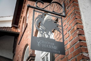 A metal sign with a rooster design and the text 'Chöner Charme Gastrikkeit' mounted on a brick wall. - Landhotel Reith  (Kuenzell)