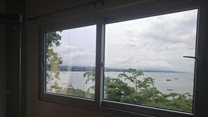 Ein Zimmer mit großem Fenster mit Blick auf ein Gewässer und viel Grün.
