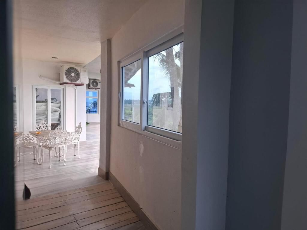 A corridor with a window, a fan, and a dining area with white chairs.