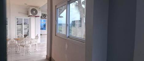 A corridor with a window, a fan, and a dining area with white chairs.