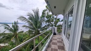 Ein Balkon mit kariertem Boden, Metallgeländer und Blick auf das Meer und Palmen.