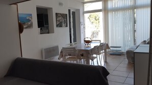 A room with a dining table, chairs, a sofa, a radiator, and a window with curtains. - Small villa sleeps 6, near the calanques.  Ideal for hiking and climbing (Marseille)