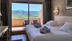 Ein Hotelzimmer mit Bett, Schreibtisch, Stuhl und einem Balkon mit Blick auf die Landschaft.