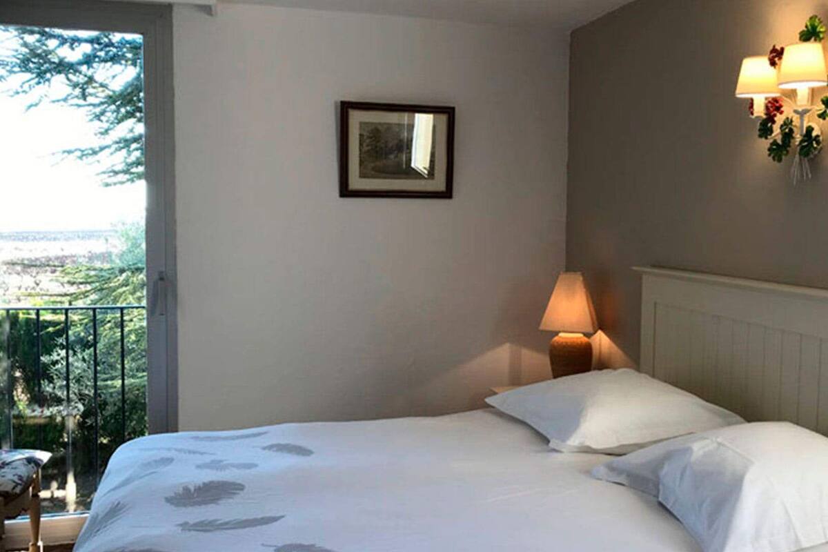 A bedroom with a bed, a nightstand, a lamp, a picture on the wall, and a balcony with a view.