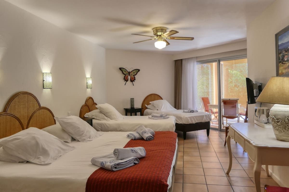 A hotel room with two beds, a ceiling fan, a table with a lamp, and a view of the outdoors.