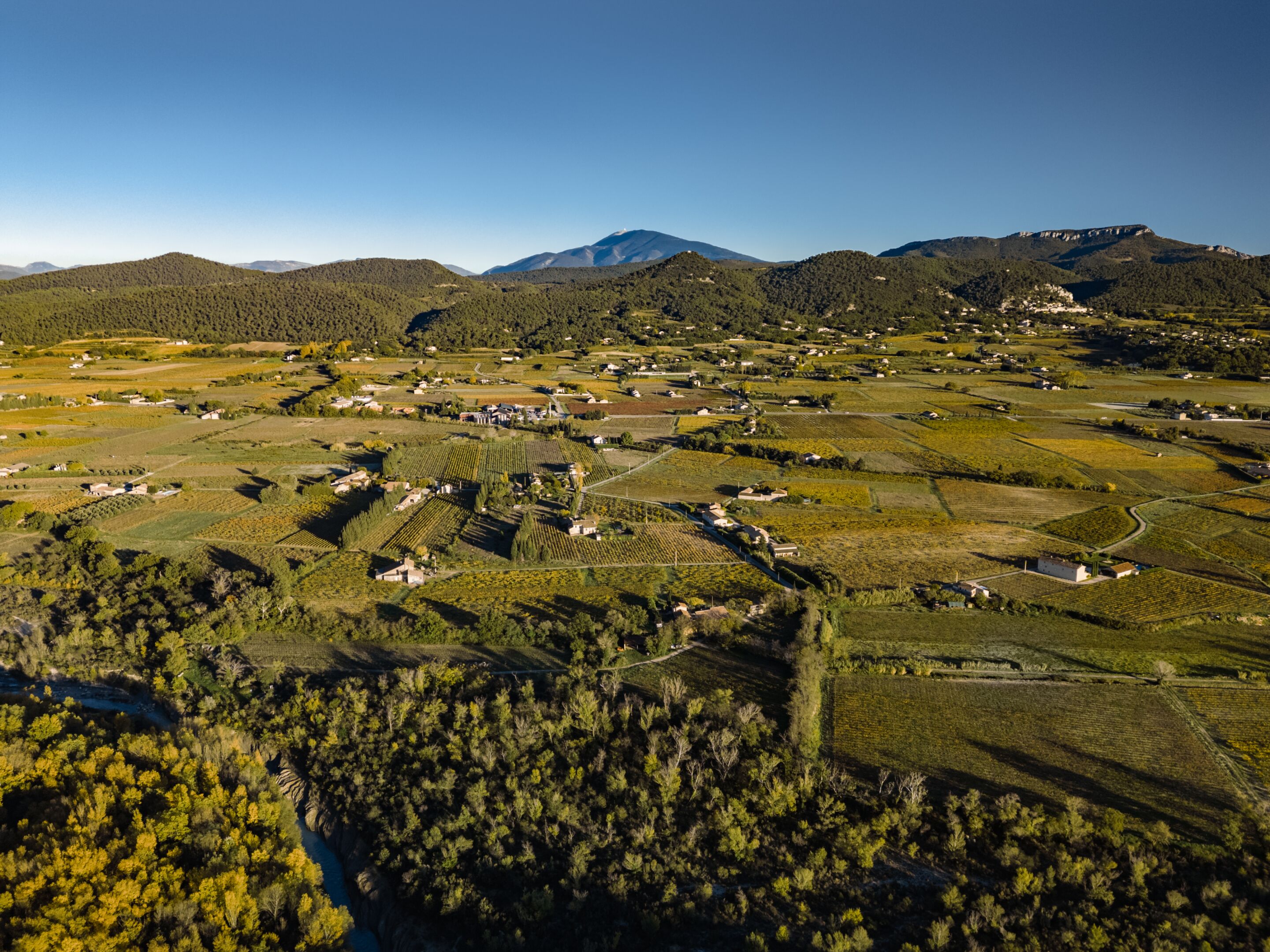 An aerial view of a rural landscape with scattered houses, fields, and a mountain range in the background.