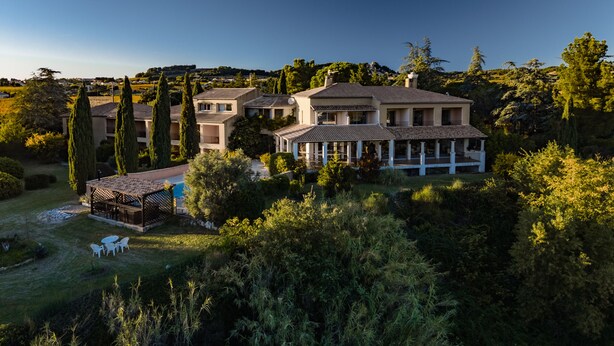 Ein großes, mehrstöckiges Haus mit Pool, umgeben von üppiger Vegetation und hohen Bäumen.