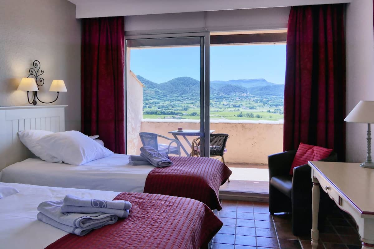 A hotel room with two beds, a balcony, a table, and a chair.