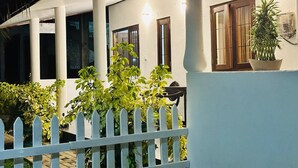 A building with a white exterior, a white picket fence, and a potted plant on the right. - KOKO Villa (Negombo)