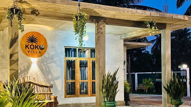 A covered outdoor area with a sign for 'KOKO VILLA,' potted plants, and a wooden bench. - KOKO Villa (Negombo)