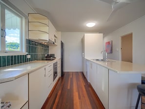 Cozinha estreita com armários brancos, pia de aço inoxidável e janela com vista para área verde.