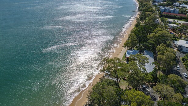 Eine Luftaufnahme einer Küstenlandschaft mit Strand, Wohngebäuden und blauem Himmel.