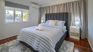 Ein Schlafzimmer mit einem Bett, einem Deckenventilator, einem Nachttisch, einem Fenster und Blick ins Freie.