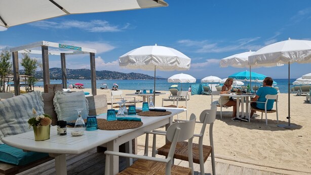 Un restaurante frente al mar con terraza, sombrillas blancas y vistas al océano.