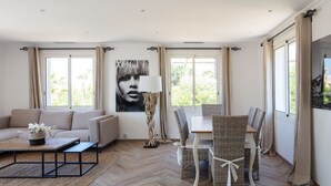 Una sala de estar con un sofá, una mesa de comedor con sillas, una lámpara y un cartel en la pared.