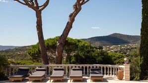 Zona junto a la piscina con sillones de descanso, una piscina con azulejos y vistas a un pueblo en la ladera.