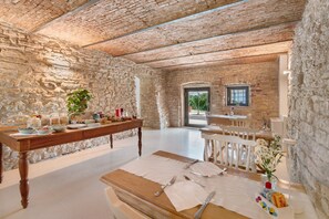 A rustic interior with stone walls, a wooden dining table set for a meal, and a view through an archway to the outside. - 'Camera Olio' with Shared Garden, Wi-Fi and Air Conditioning (Negrar di Valpolicella)
