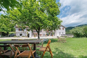 A patio with a table and chairs, a tree, and a building in the background. - Wine Room with Shared Garden, Wi-Fi and Air Conditioning (Negrar di Valpolicella)