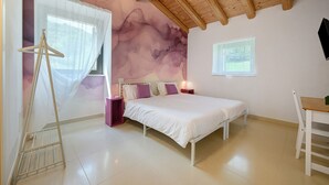 Un dormitorio con cama, mesitas de noche, una silla, un perchero y una ventana.