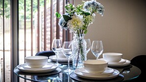 Uma mesa posta com tigelas, pratos e copos de vinho brancos, com um vaso de flores ao centro.