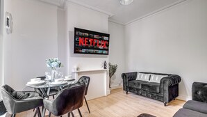 Uma sala de estar moderna com área de refeições, um sofá de couro preto e uma TV de tela plana exibindo o logotipo da Netflix.