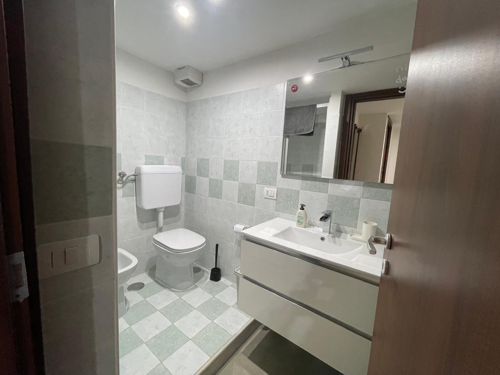 A bathroom with a toilet, sink, mirror, and tiled floor.