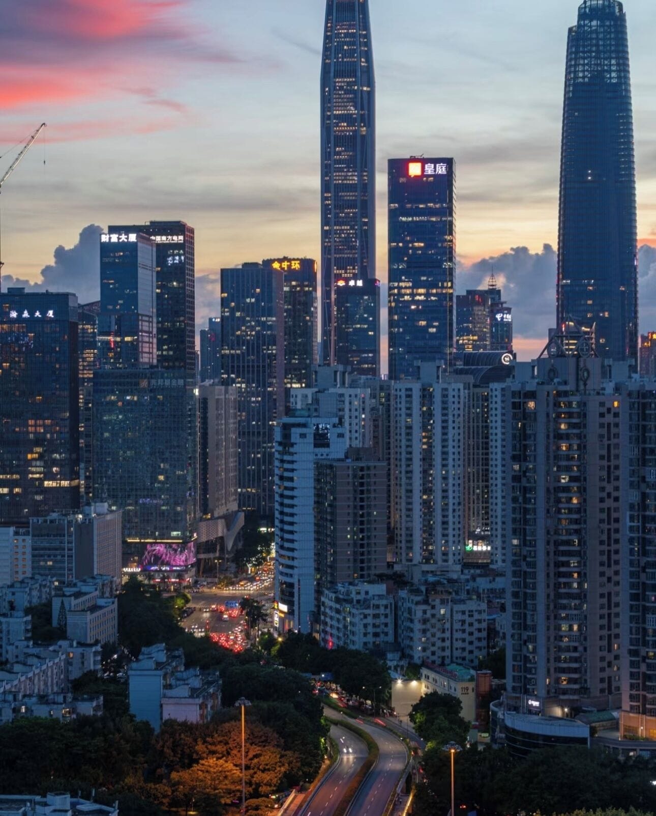 A cityscape with high-rise buildings, a curved road, and a sunset sky.