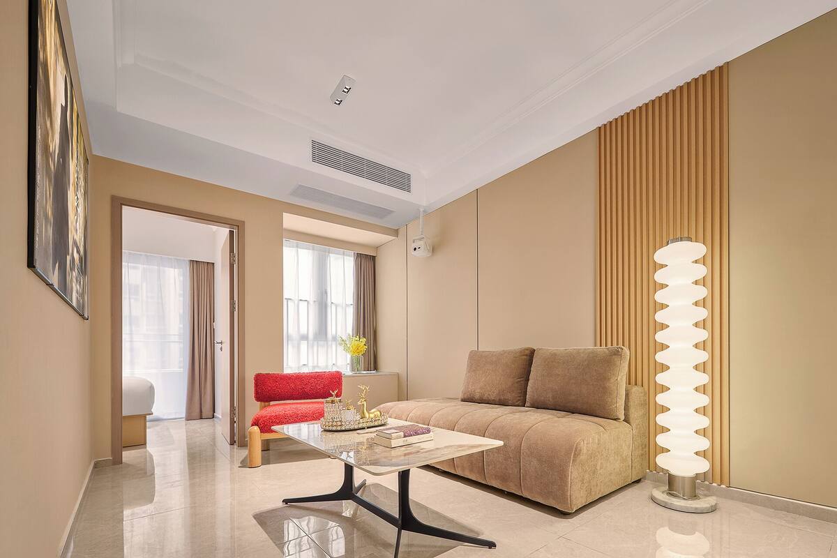 Una habitación de hotel moderna con sofá, una mesa de centro, una lámpara y un cuadro en la pared.