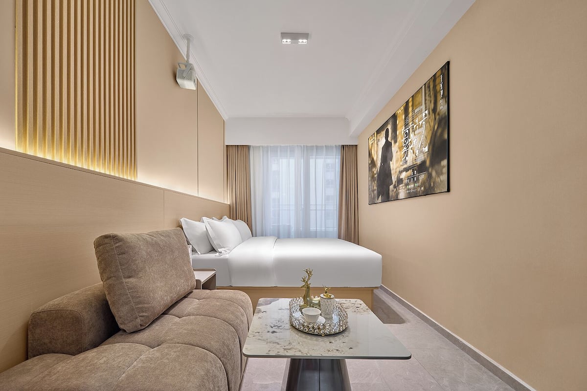 Habitación de hotel con cama, sofá, una mesita con bandeja y proyector instalado en la pared.