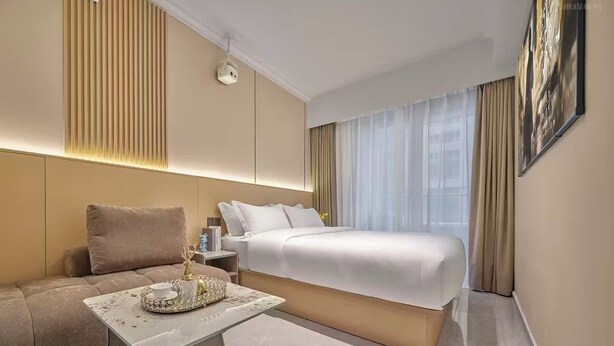 A hotel room with a bed, a sofa, a small table, and a wall-mounted security camera.